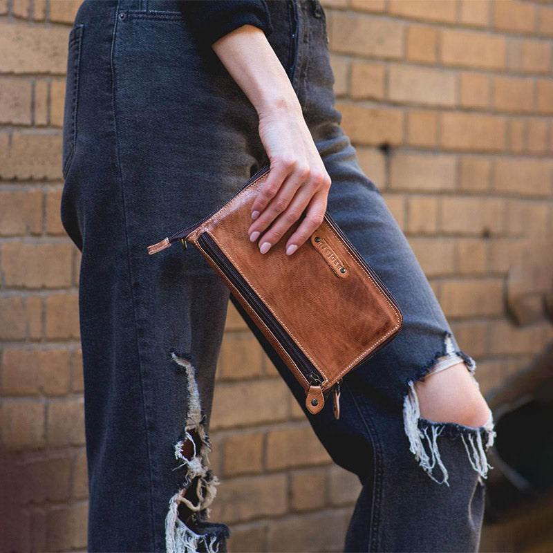 Girl wearing black ripped jeans holding a brown leather wallet.