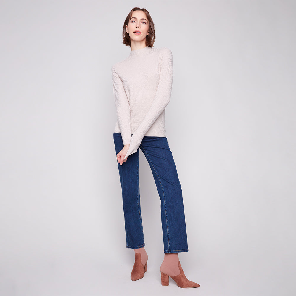 Woman wearing a white sweater and blue jeans on a plain background