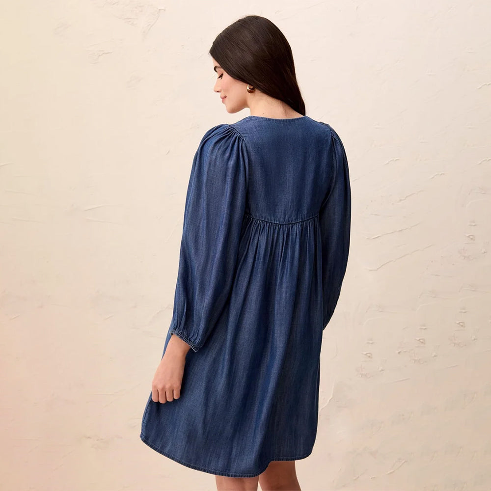A woman wearing a dark blue denim dress, shown from the back against a textured beige wall.