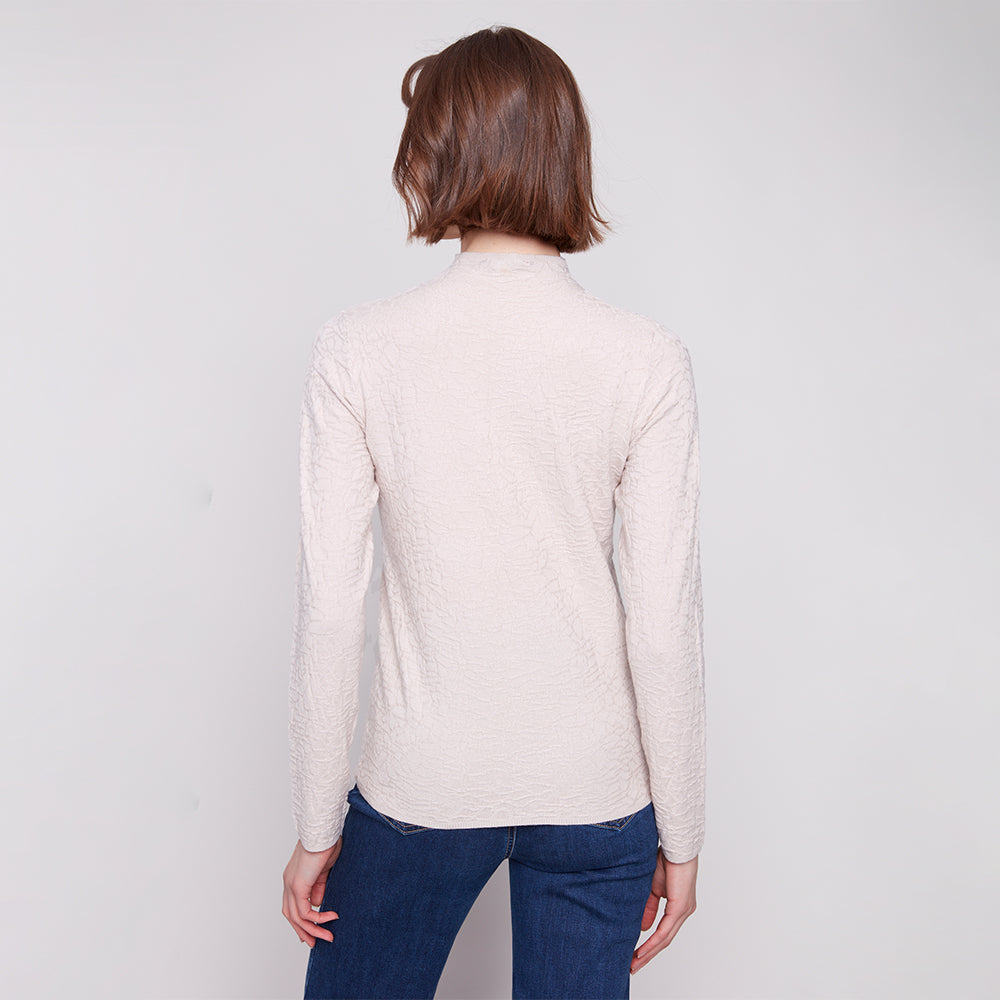 Person wearing a beige sweater and blue jeans on a plain background