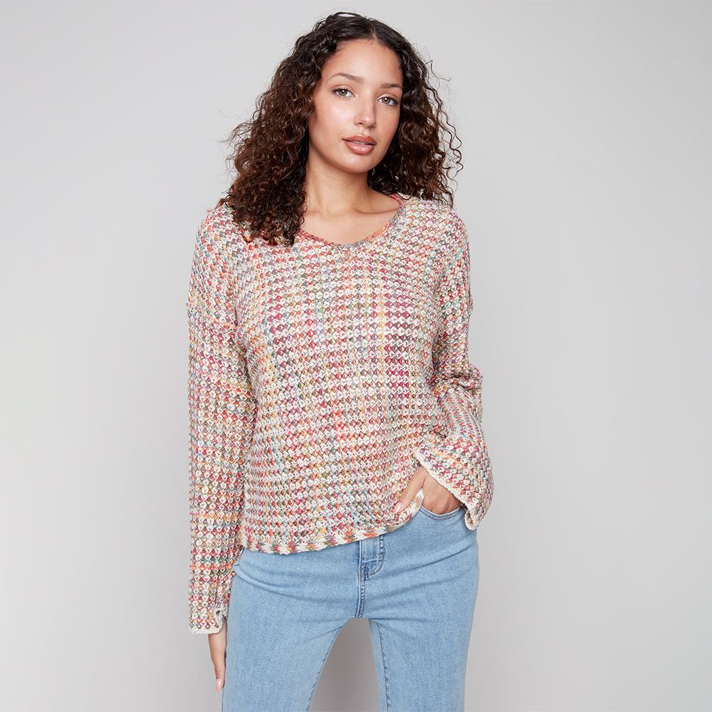 Woman wearing a patterned long-sleeve top and blue jeans against a plain background