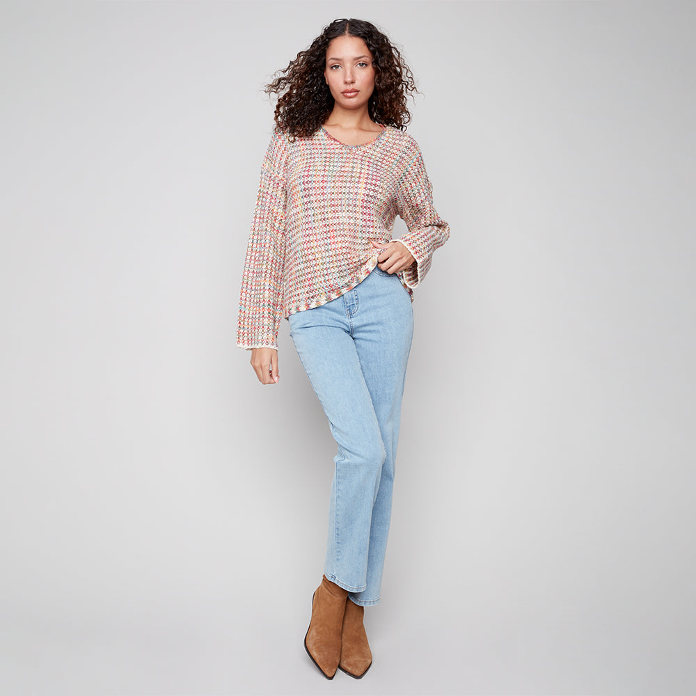 Woman wearing a patterned blouse and light blue jeans against a plain background