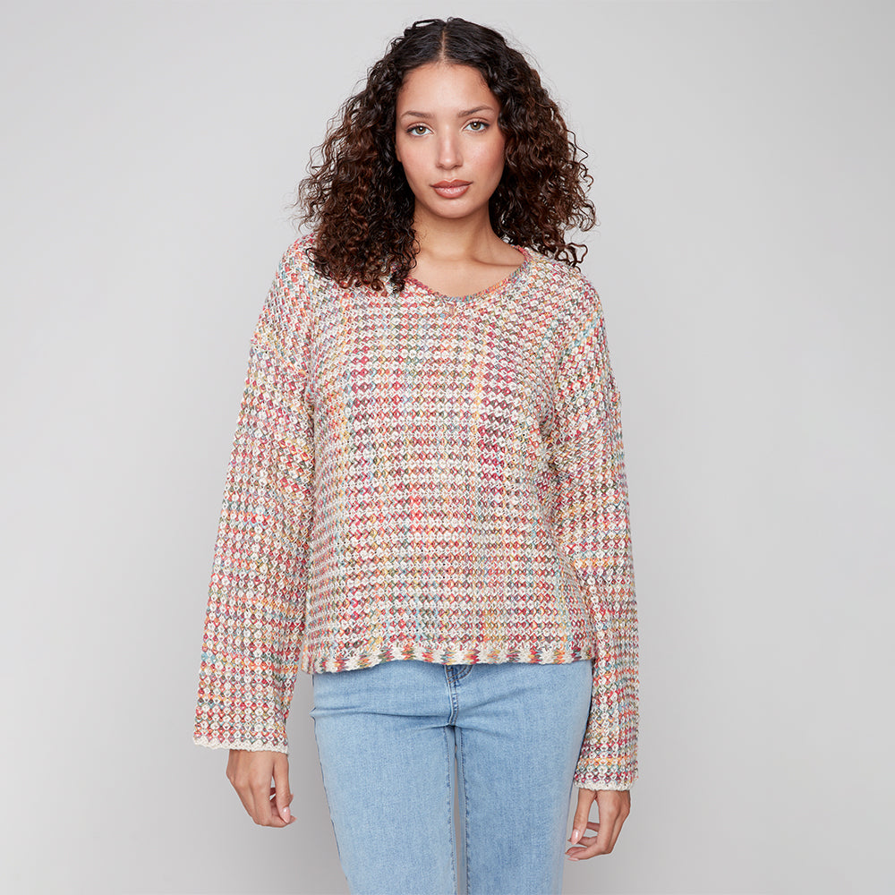 Woman wearing a patterned sweater and light blue jeans against a plain background