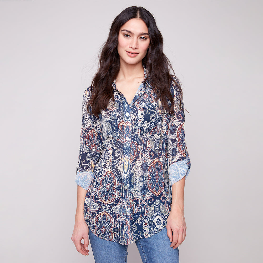 Woman wearing a patterned shirt and jeans on a plain background