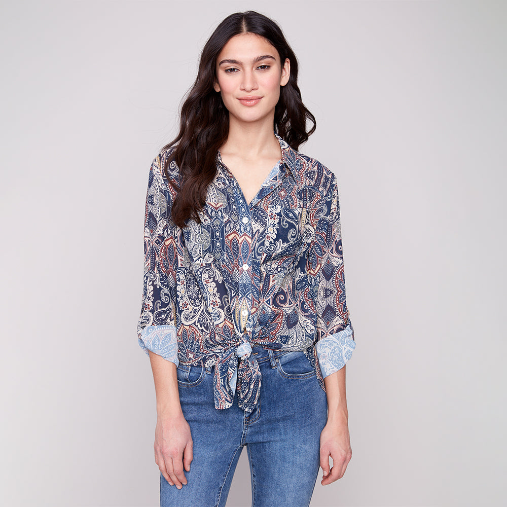 Woman wearing a patterned shirt and jeans on a plain background