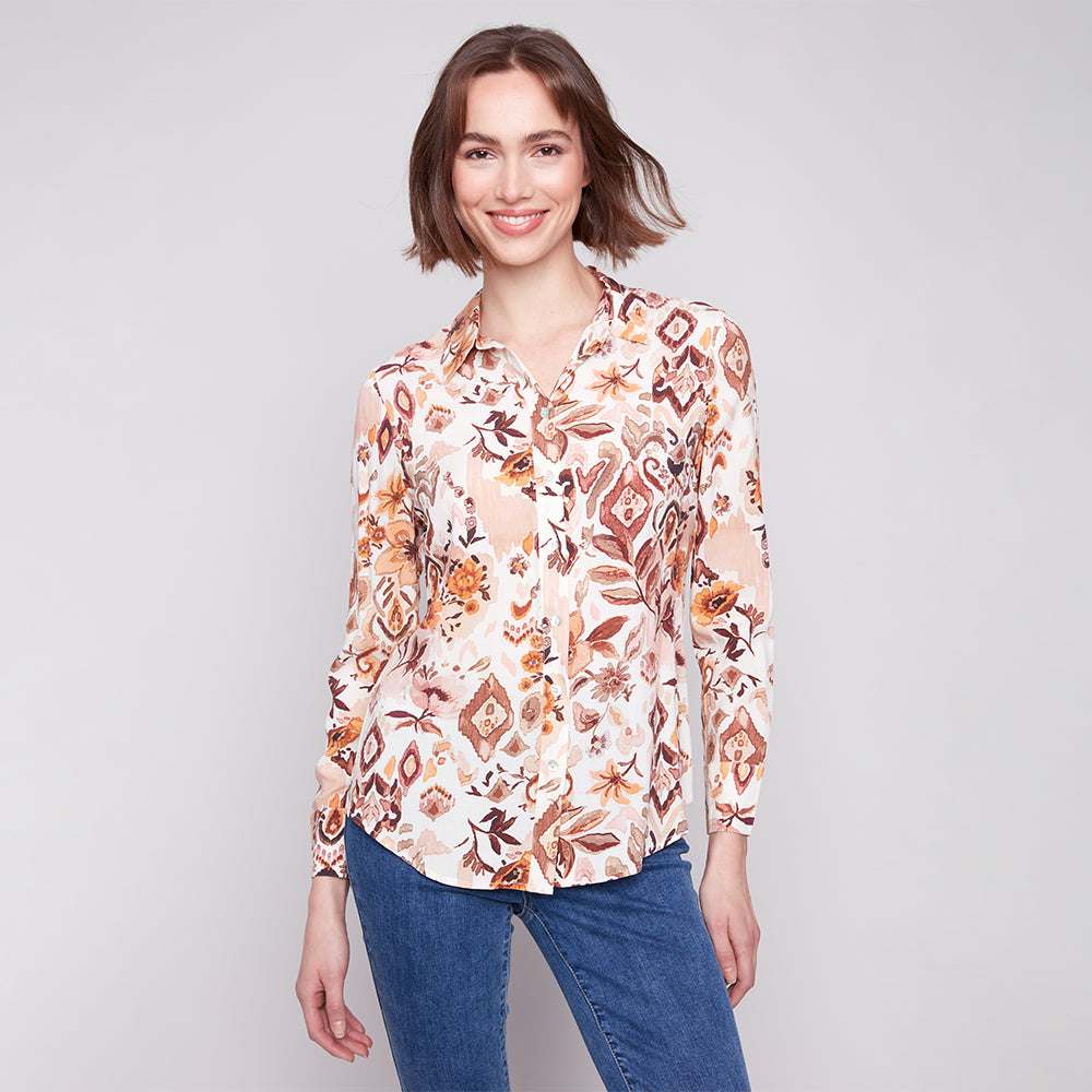 Woman wearing a patterned blouse and blue jeans on a plain background