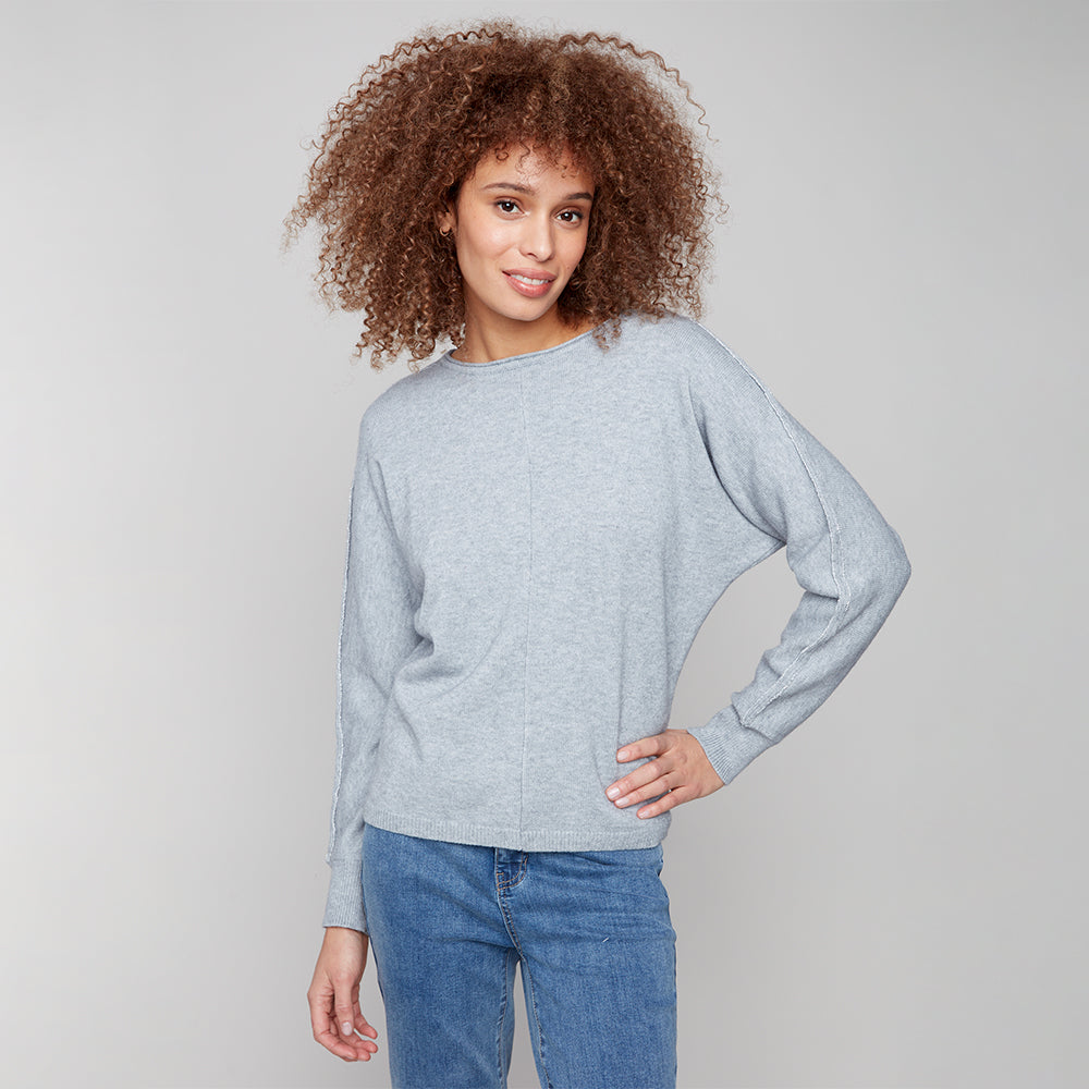 Woman wearing a light blue sweater and blue jeans against a plain background