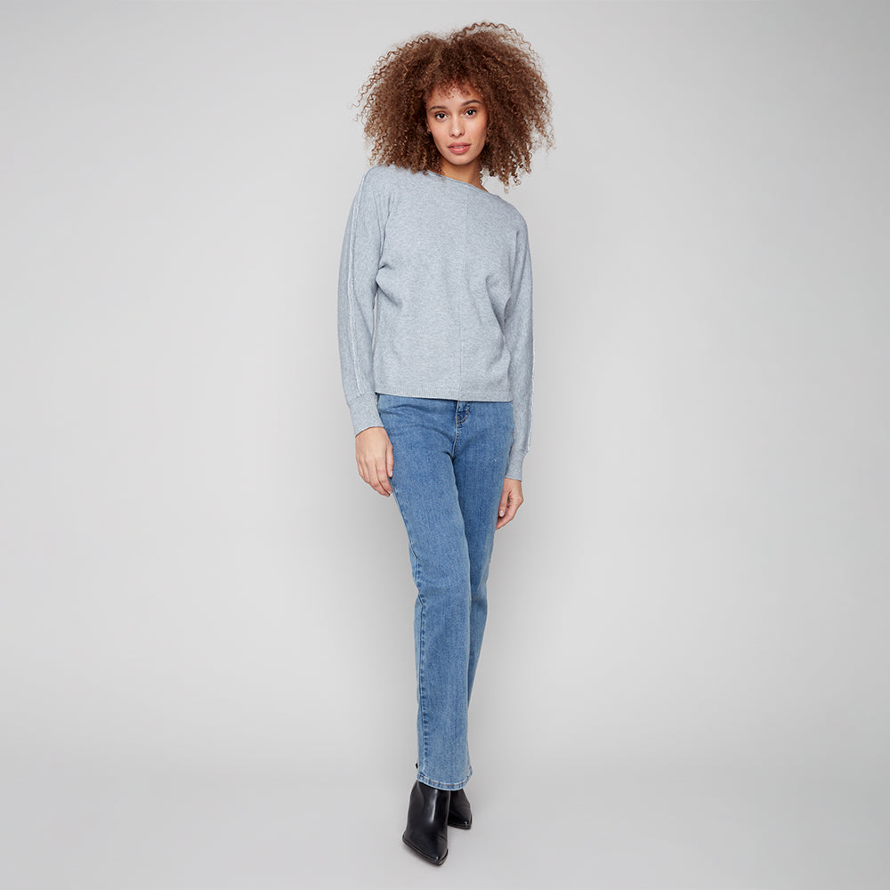 Woman wearing a light gray sweater and blue jeans on a plain background