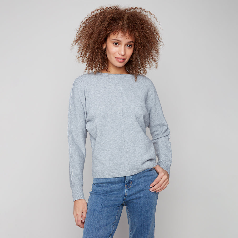 Woman wearing a light gray sweater and blue jeans against a plain background