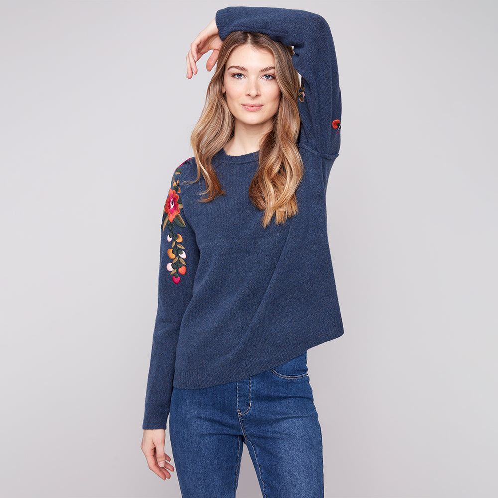 Woman wearing a blue sweater with floral embroidery on a gray background