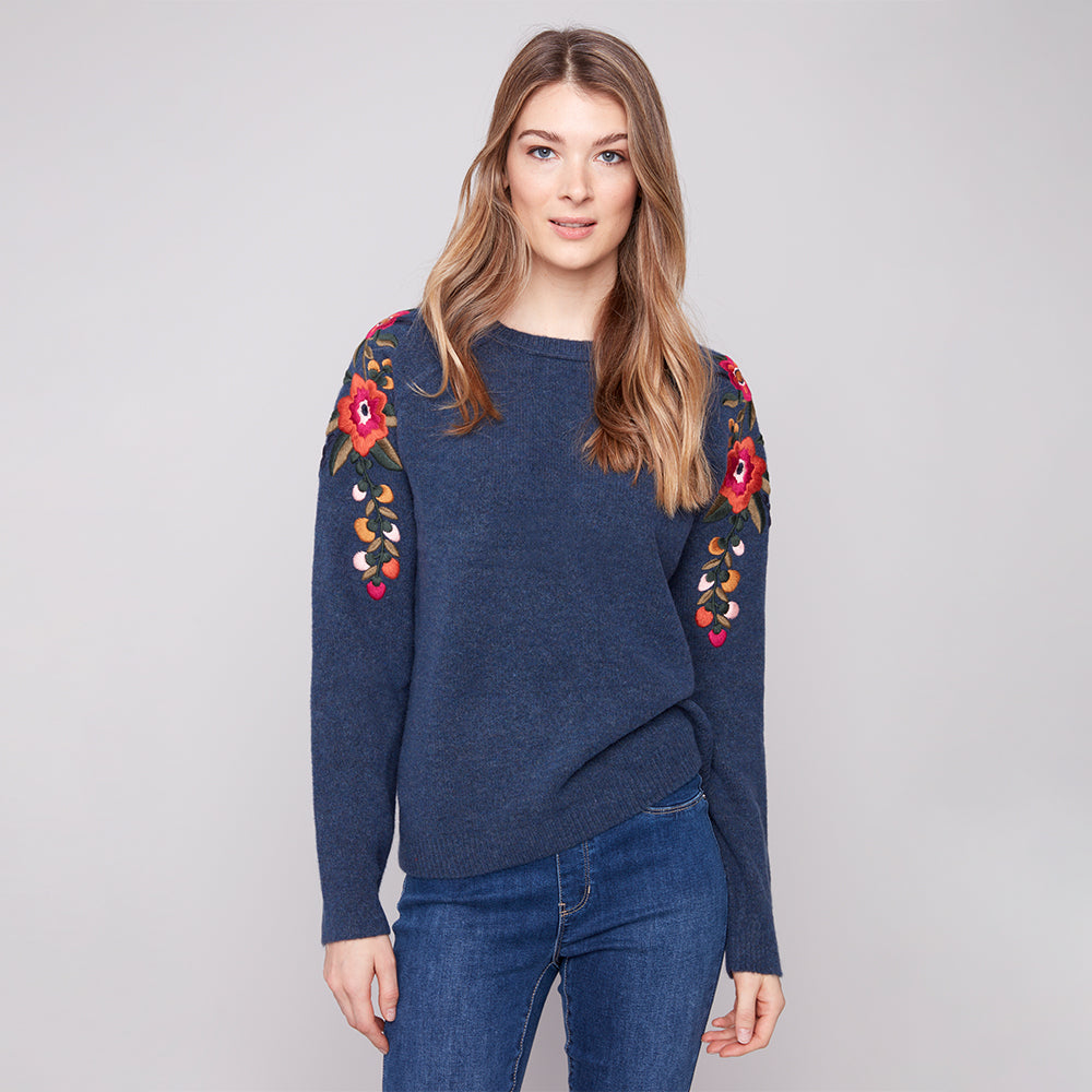 Woman wearing a blue sweater with floral embroidery on a gray background
