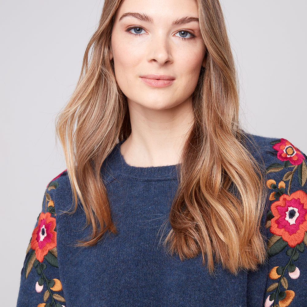 Woman wearing a blue sweater with floral patterns on a plain background