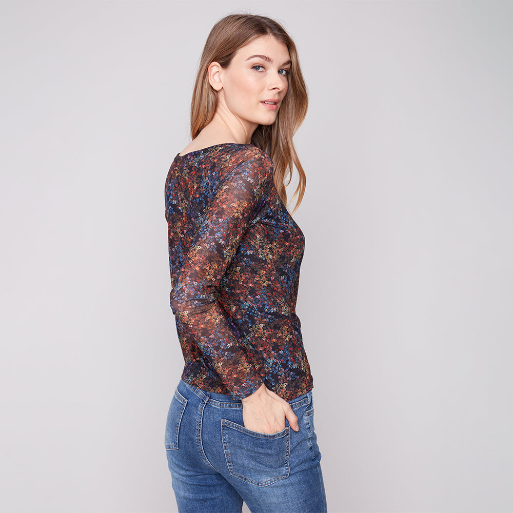 Woman wearing a floral long-sleeve top and jeans on a plain background