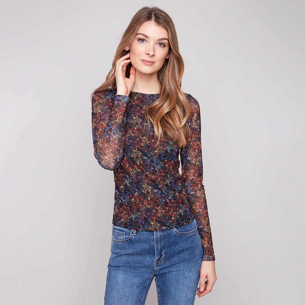 Woman wearing a floral long-sleeve top and blue jeans on a plain background