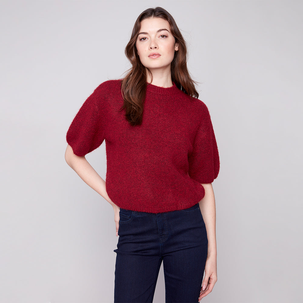 Woman wearing a red sweater and dark pants against a gray background