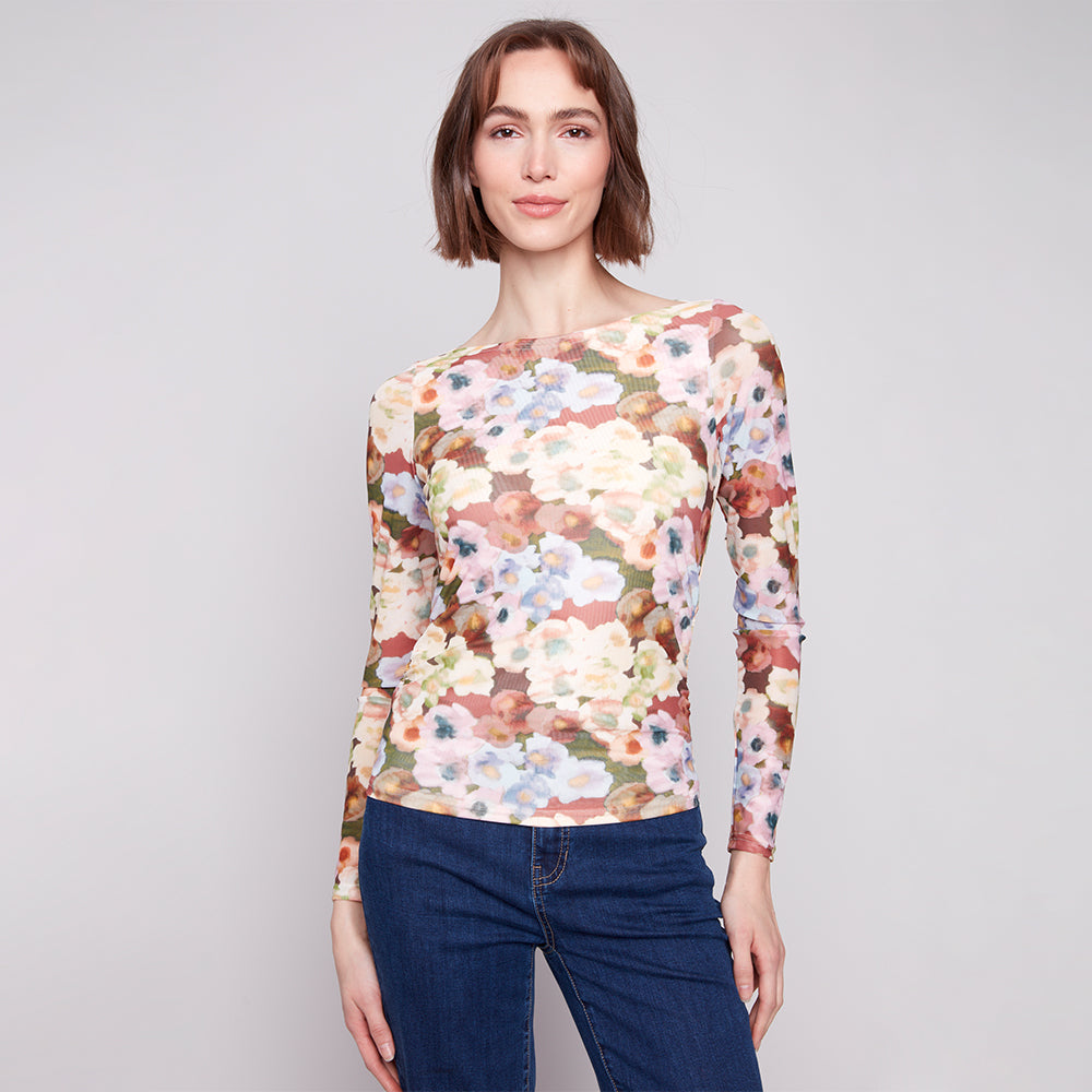 Woman wearing a floral long-sleeve top and blue jeans on a gray background