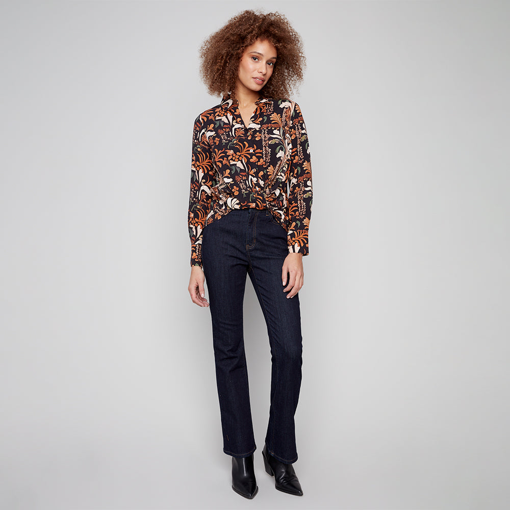 Woman wearing a patterned blouse and dark jeans on a gray background