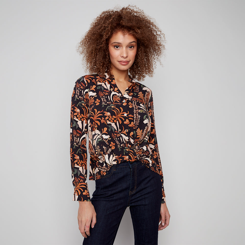 Woman wearing a patterned blouse and dark jeans against a plain background