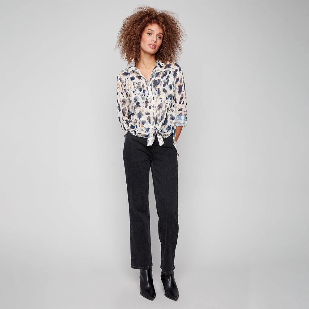 Woman wearing a patterned blouse and black pants on a gray background