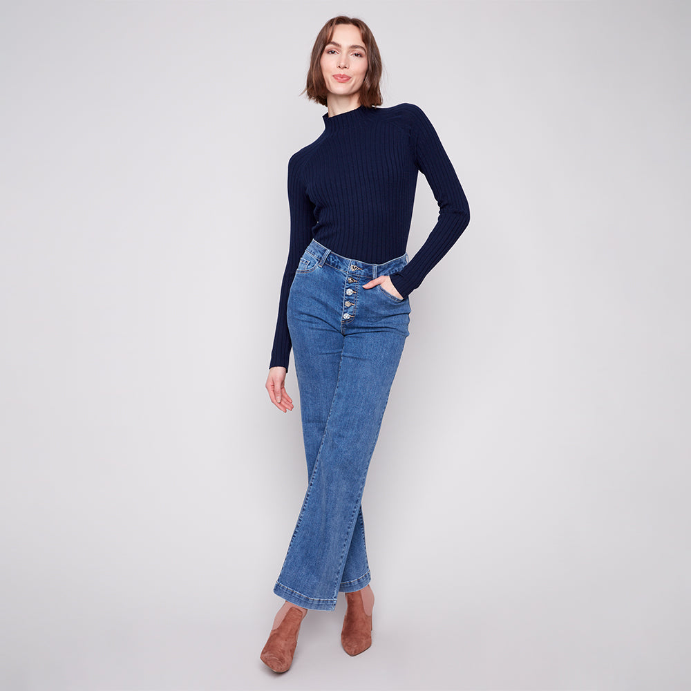 Woman wearing a navy ribbed sweater and blue jeans on a white background