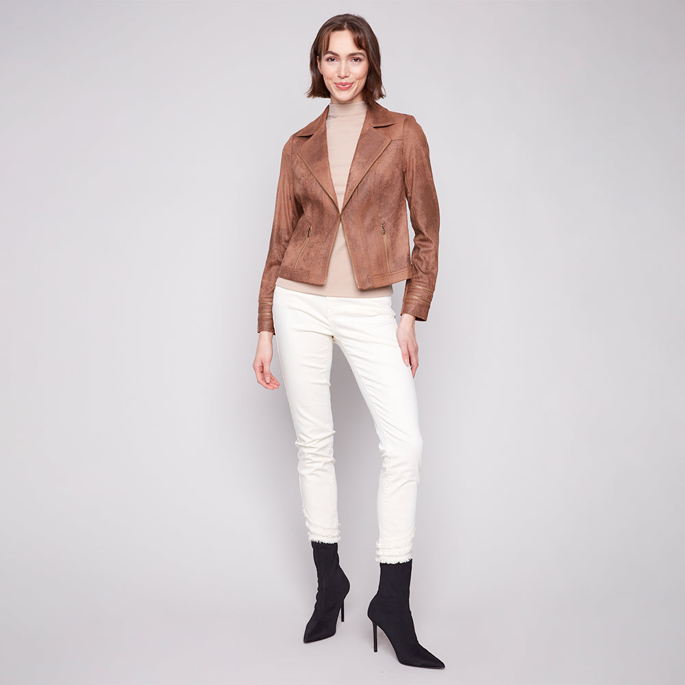 Woman wearing a brown leather jacket, white pants, and black high-heeled boots on a light gray background