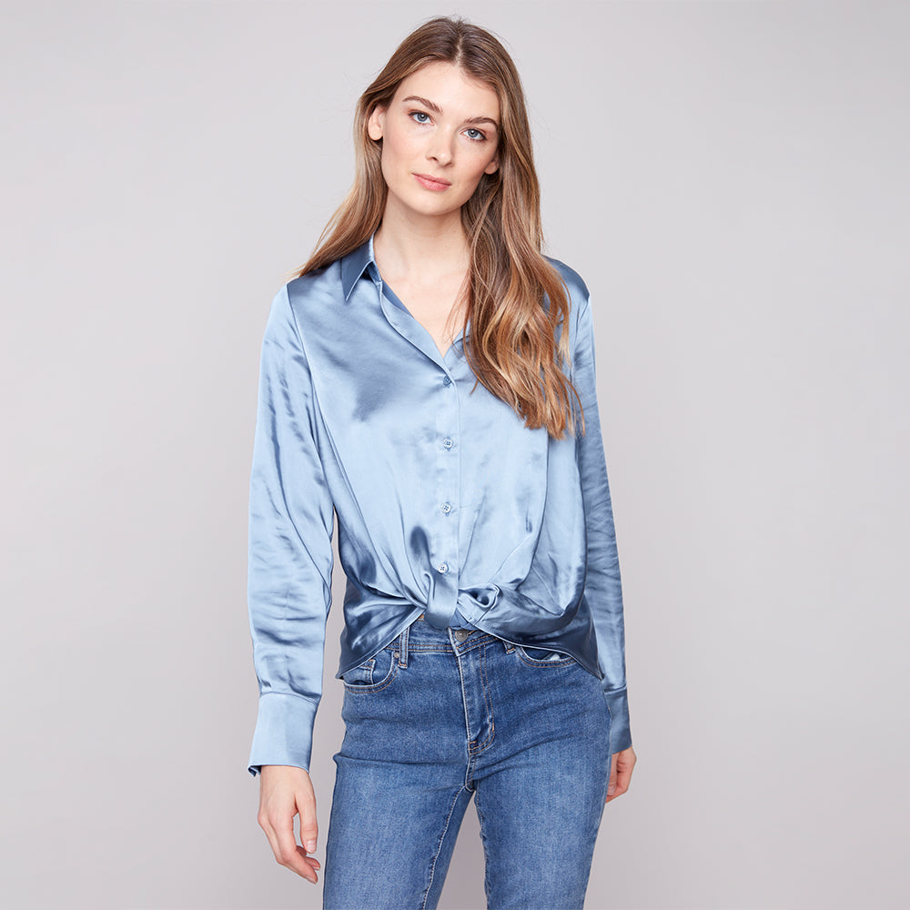 Woman wearing a blue satin shirt and jeans against a gray background