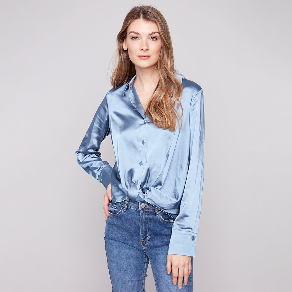 Woman wearing a light blue satin shirt and jeans on a plain background