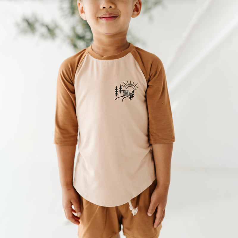 A child wearing a beige and brown 3/4 sleeve baseball tee with a graphic on the front.