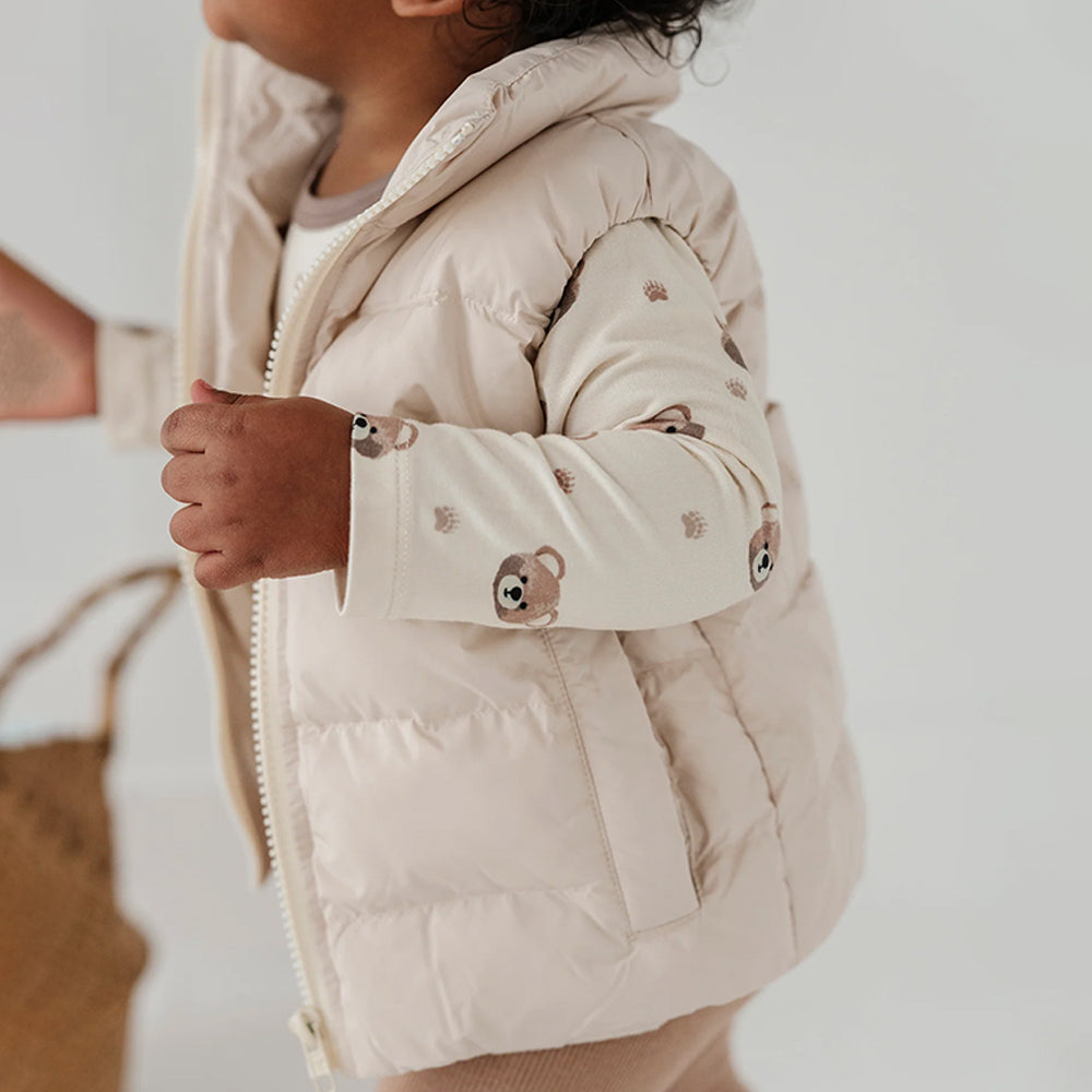 Child wearing a beige puffer jacket with bear designs on a neutral background