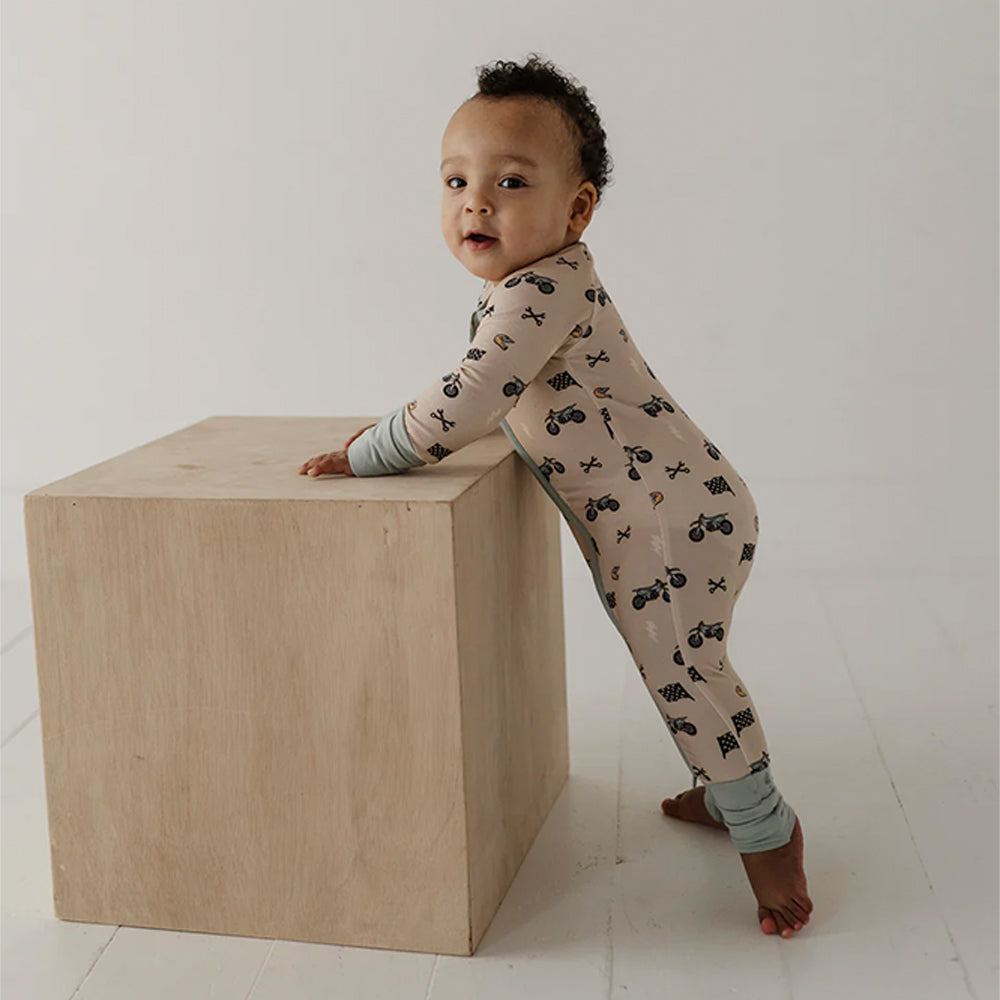 Child in a patterned onesie standing on a wooden block against a white background