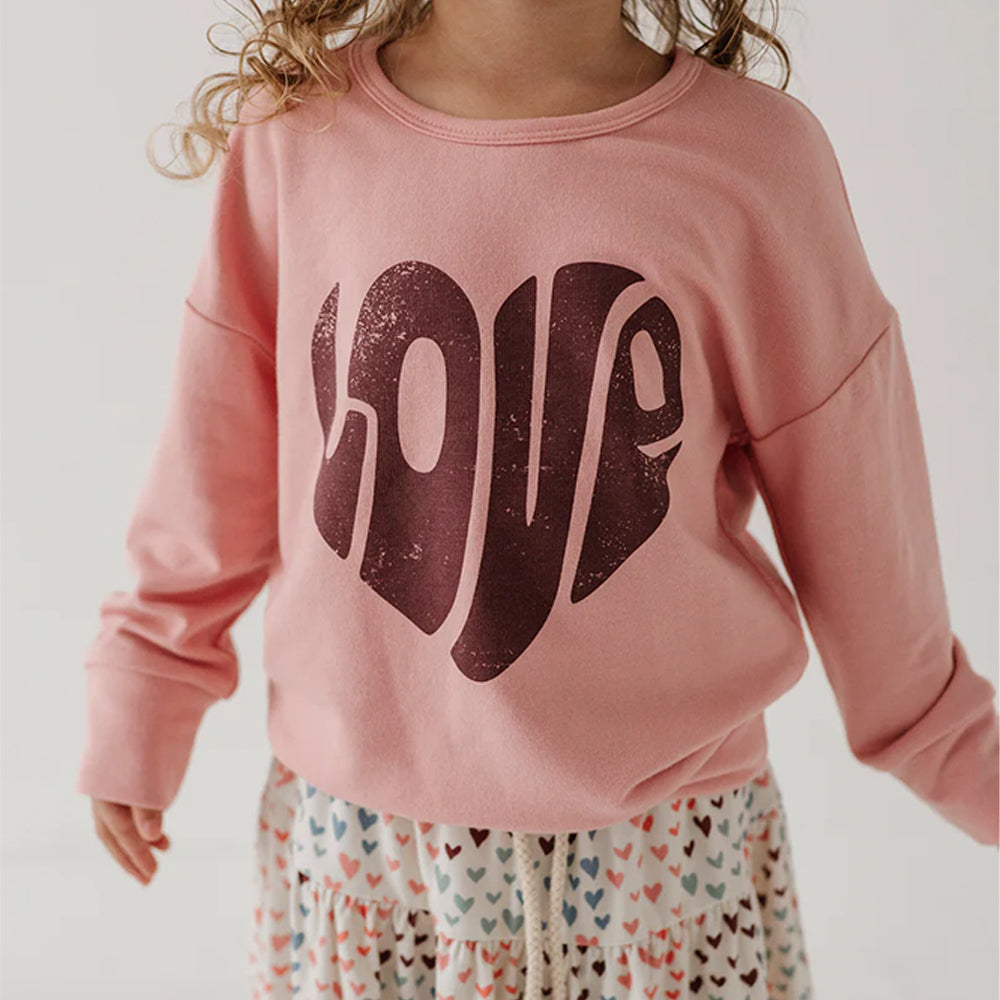 Child wearing a pink sweatshirt with 'LOVE' printed on it against a plain background
