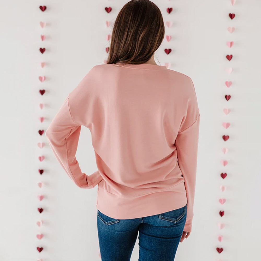 Person wearing a pink long-sleeve top in front of a heart-patterned wall.