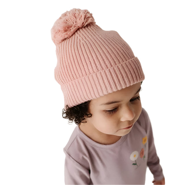 Child wearing a pink knit beanie with a pom-pom on a plain background