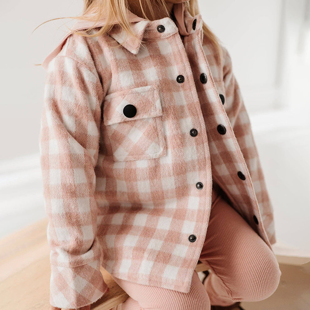 Person wearing a pink and white checkered jacket with black buttons on a light background