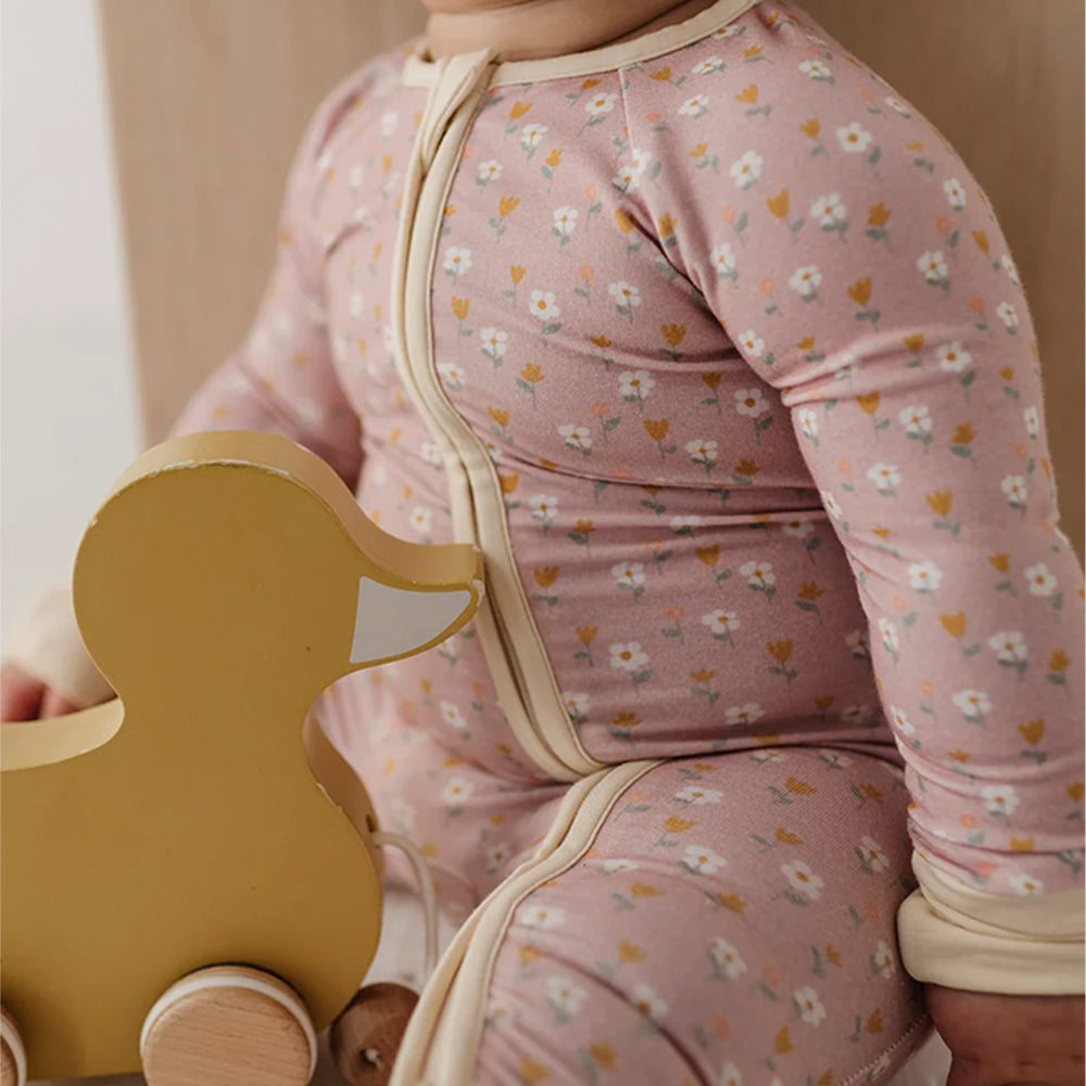 Child wearing a pink floral outfit holding a yellow wooden toy.