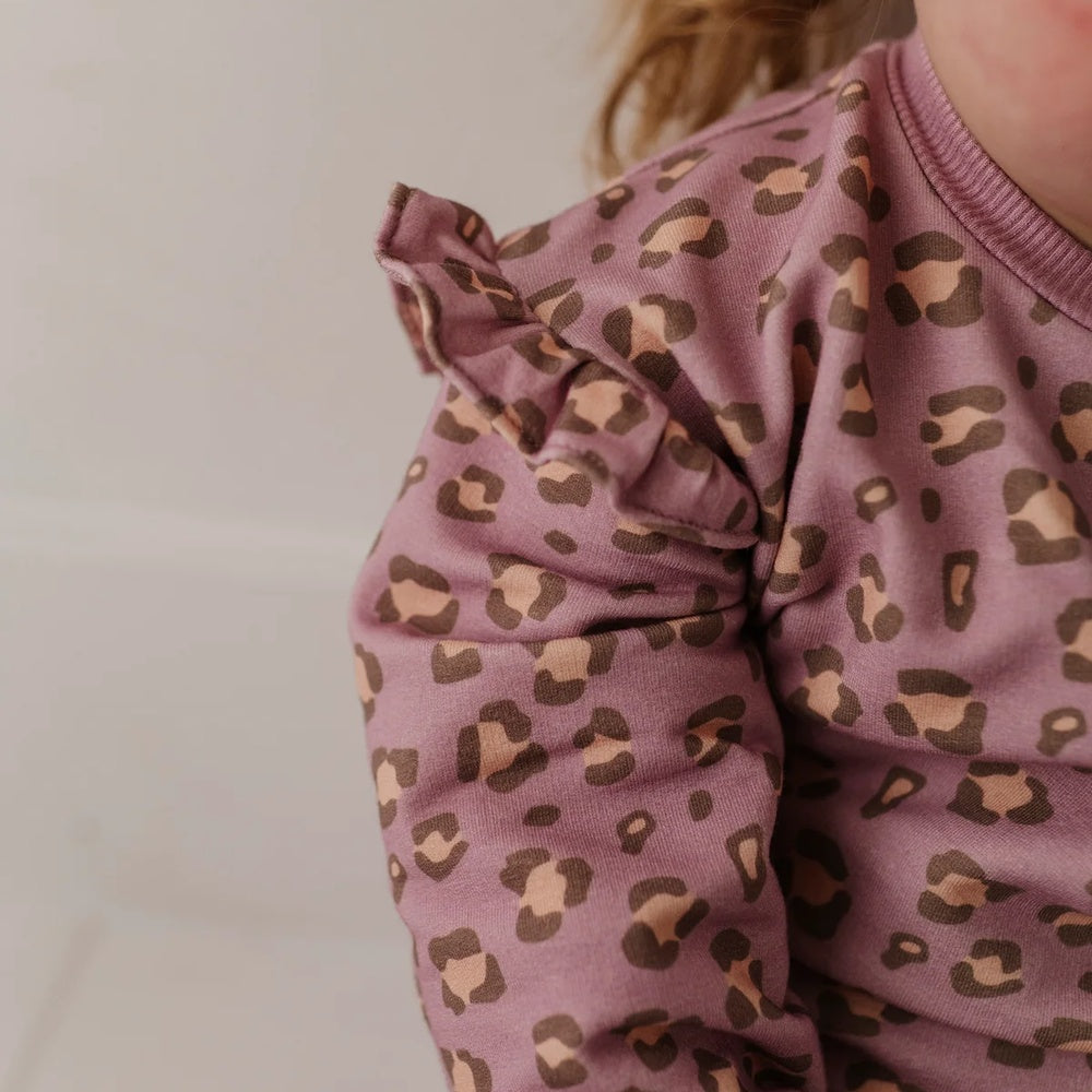 Close-up of a child wearing a dusty mauve long-sleeve top with a brown and beige leopard print, featuring ruffled detailing on the shoulder.
