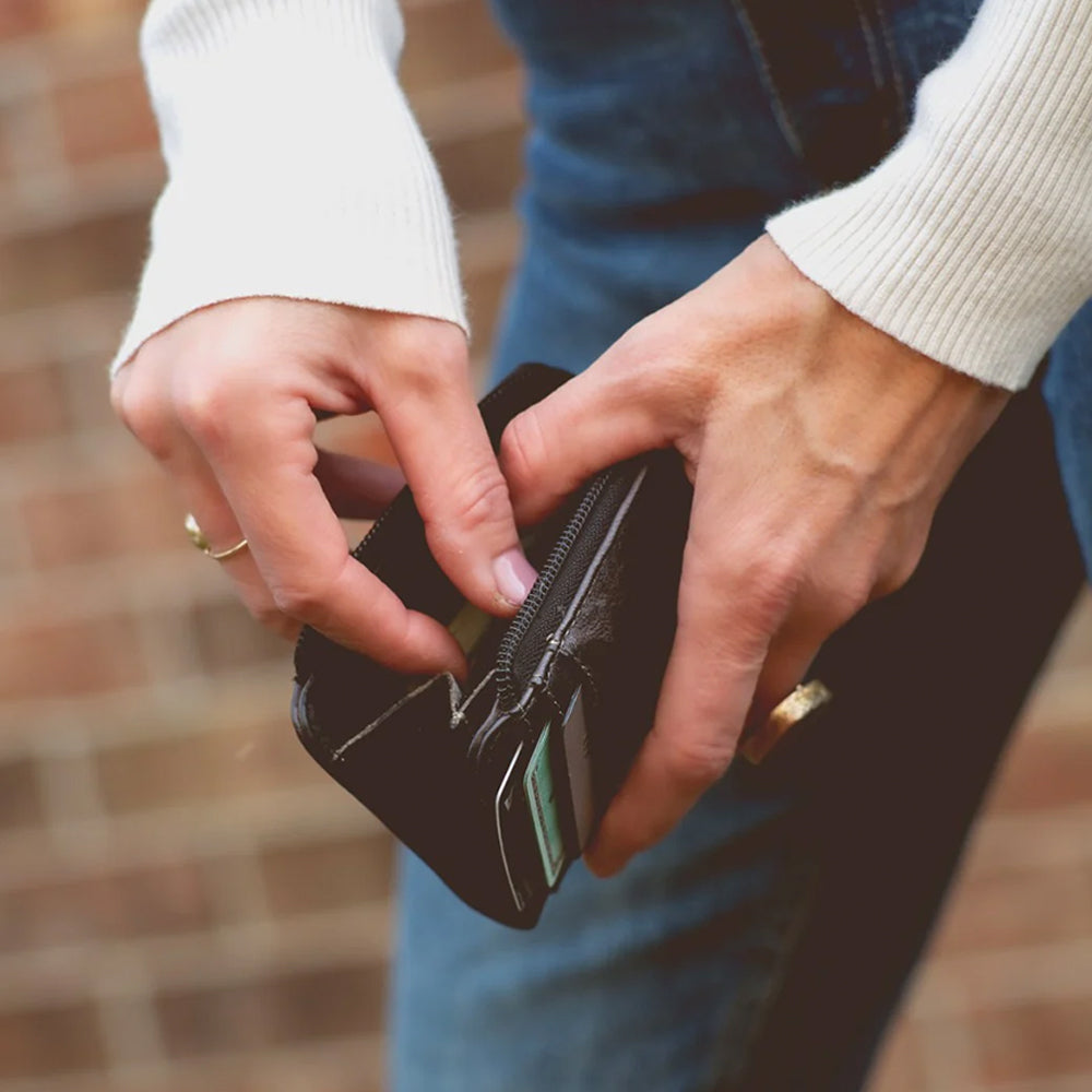 Close-up of hands opening a black wallet with a blurred brick wall background