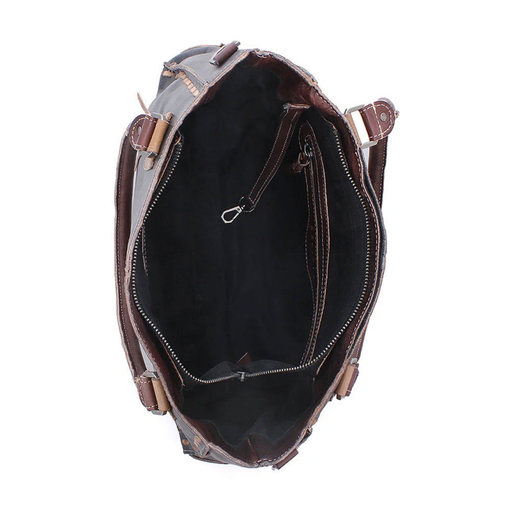 An overhead view of an open brown leather tote bag, showing a black fabric interior with zipper compartments and side strap attachments, set against a plain white background.