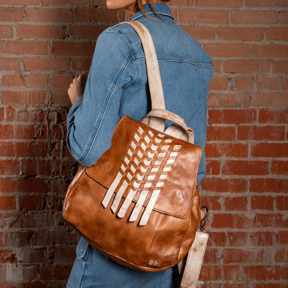 Person wearing a brown leather backpack with a geometric design against a brick wall.