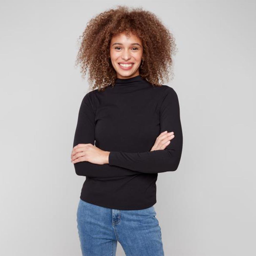 Woman wearing a black turtleneck and blue jeans against a gray background