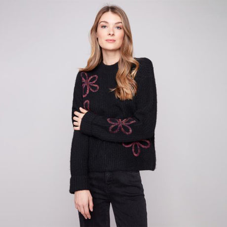 Woman wearing a black sweater with pink floral patterns on a gray background