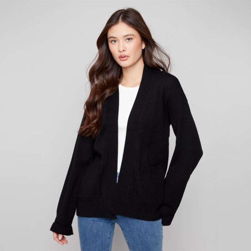 Woman wearing a black cardigan over a white shirt with blue jeans on a gray background