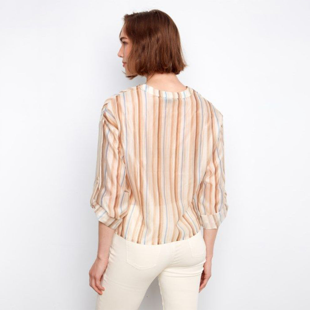 Woman wearing a striped shirt and white pants against a plain background