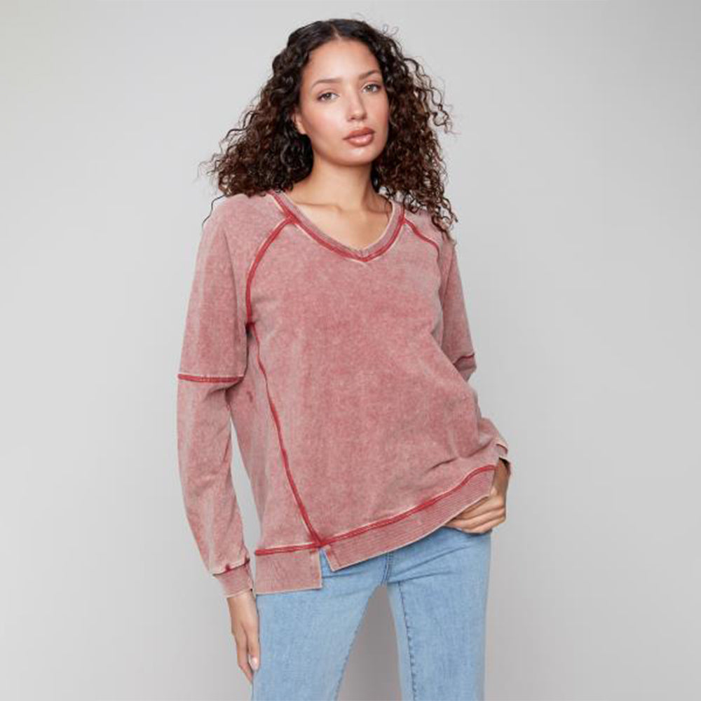 Woman wearing a pink sweatshirt and blue jeans against a gray background