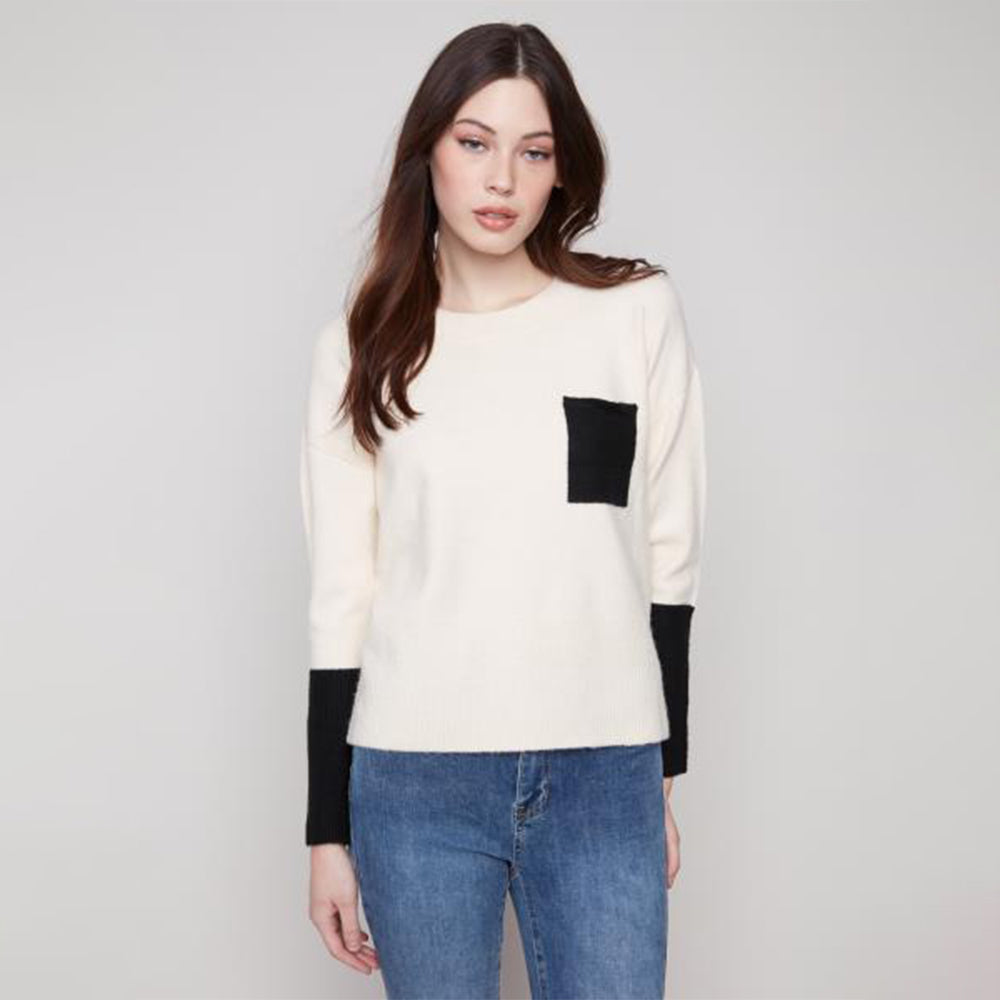 Woman wearing a white sweater with black sleeves and blue jeans on a plain background