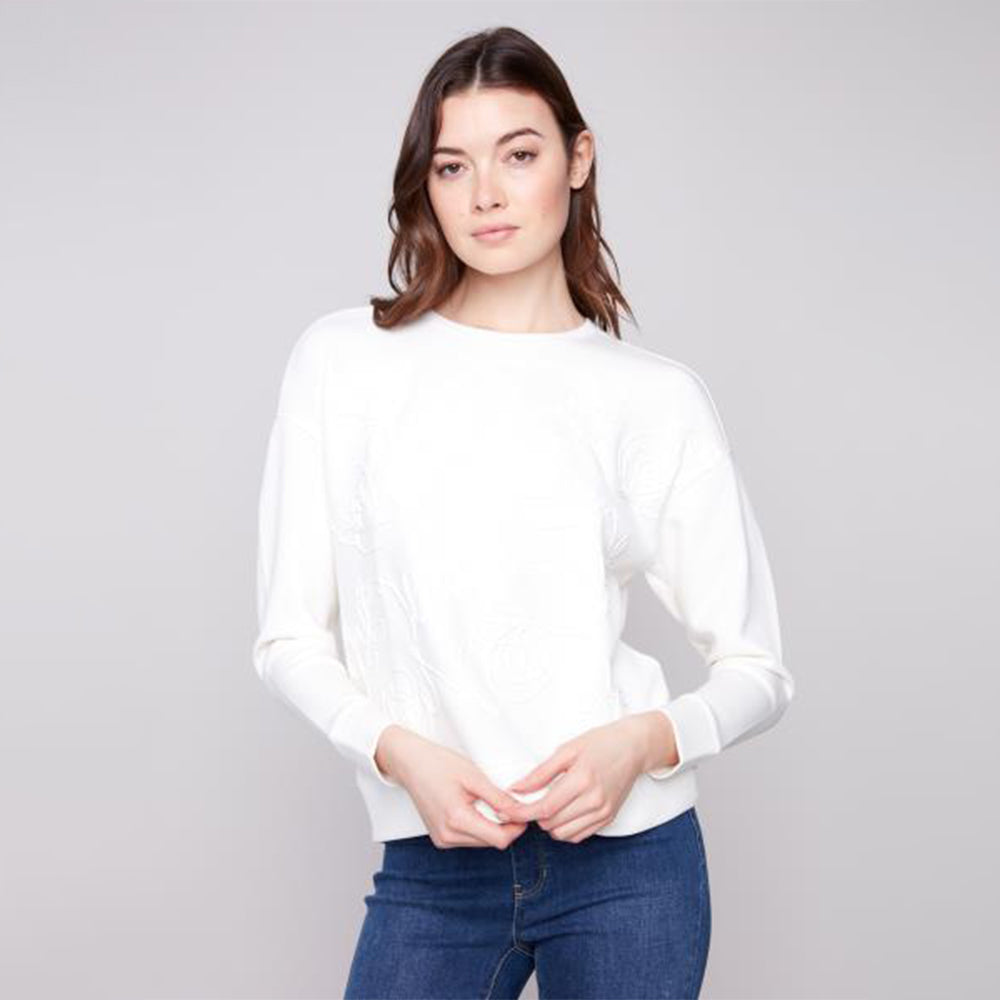 Woman wearing a white sweater and blue jeans against a gray background
