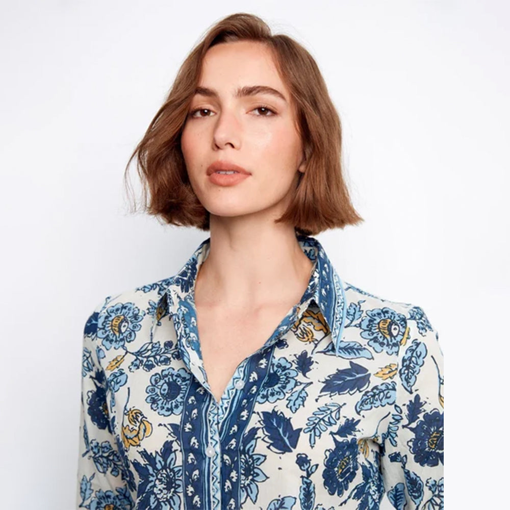 A woman with a short brown bob hairstyle wearing a blue and navy floral print button-up shirt, photographed against a clean white background.