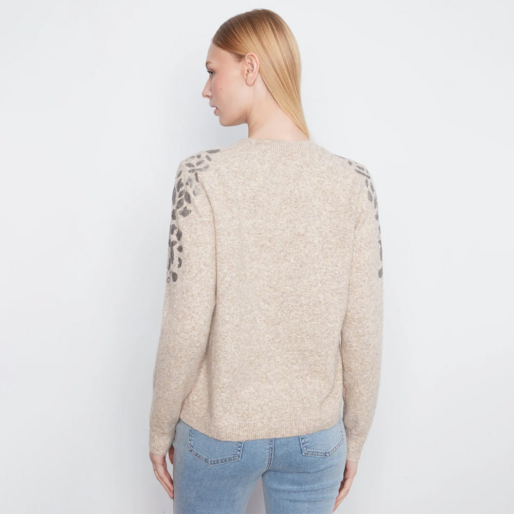 A woman shown from the back wearing a beige knit sweater with dark gray leopard print detailing on the upper sleeves, paired with light blue jeans, against a plain white background.