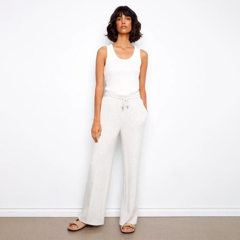 Woman wearing a white sleeveless top and wide-leg pants against a plain background