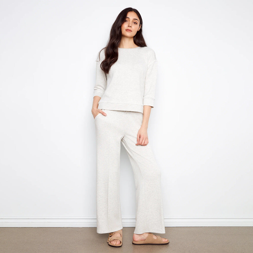 Woman wearing a white outfit standing against a plain white wall.